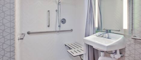 Un baño moderno con cabina de ducha, barra de apoyo y lavabo con espejo.