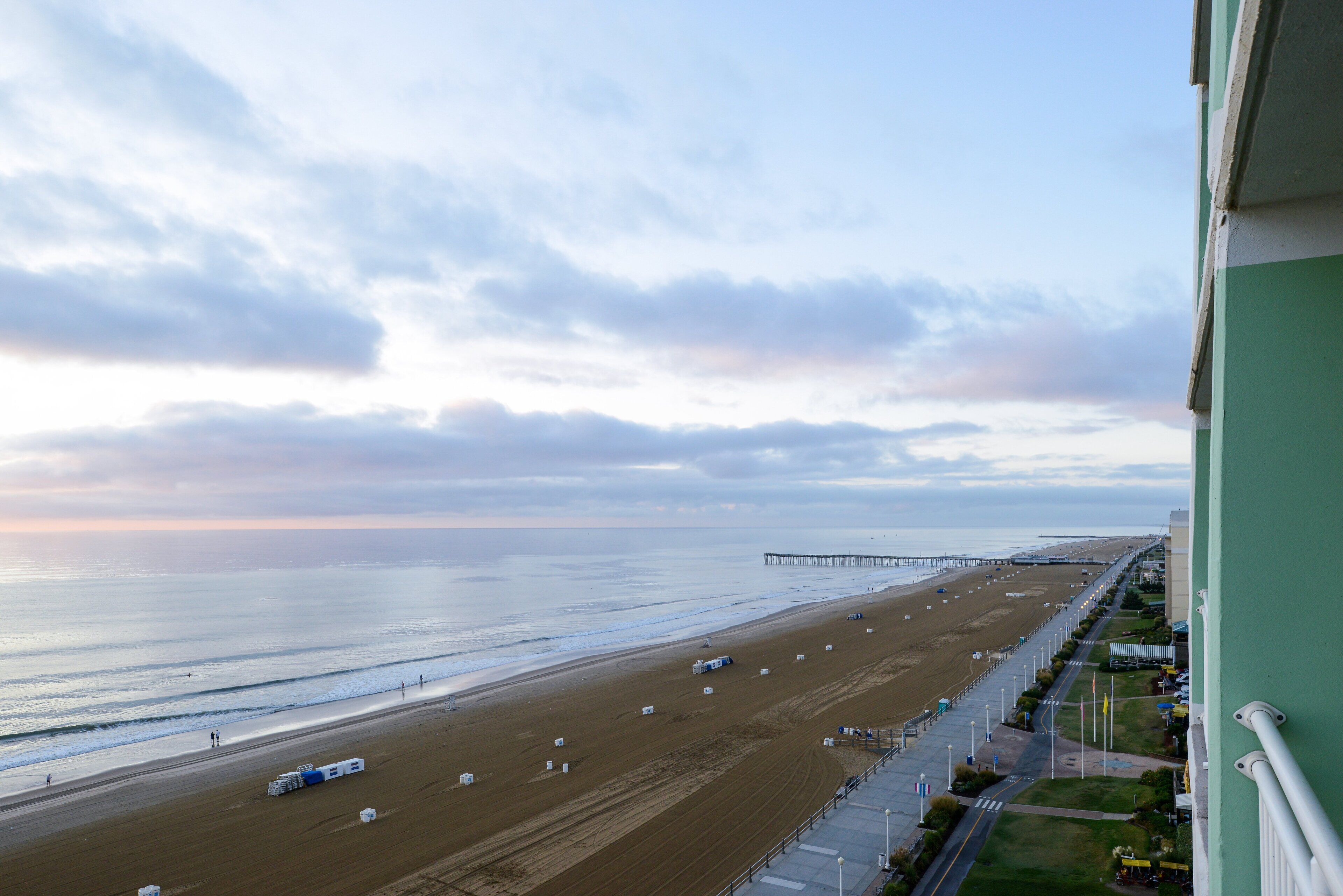 A beach view from a balcony with a pier in the distance.