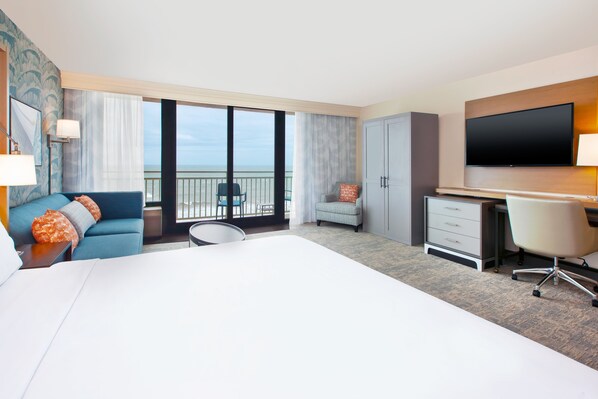 Una habitación de hotel con una cama grande, un escritorio, una silla, un sofá, un televisor y un balcón con vistas.