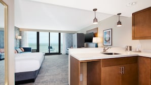 Quarto de hotel moderno com uma cama grande, uma cozinha compacta, uma varanda com vista e uma televisão.