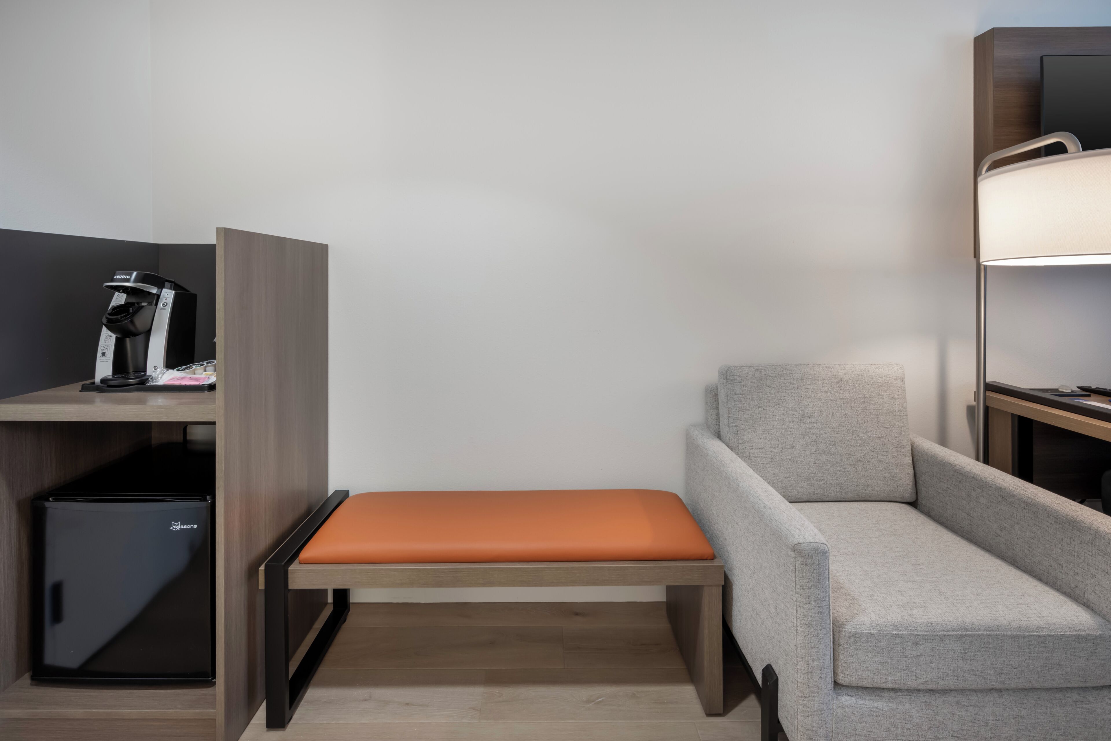 Habitación de hotel pequeña con una cama individual, un escritorio, una cafetera y un espacio de almacenamiento.