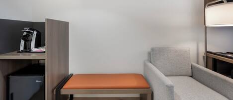 A compact hotel room with a single bed, a small desk, a coffee machine, and a storage unit.