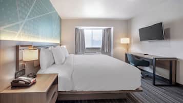 A hotel room with a bed, desk, chair, TV, and window.