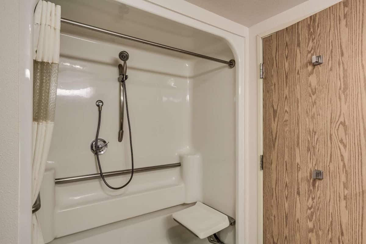 A shower with a grab bar, a white towel, and a wooden door.