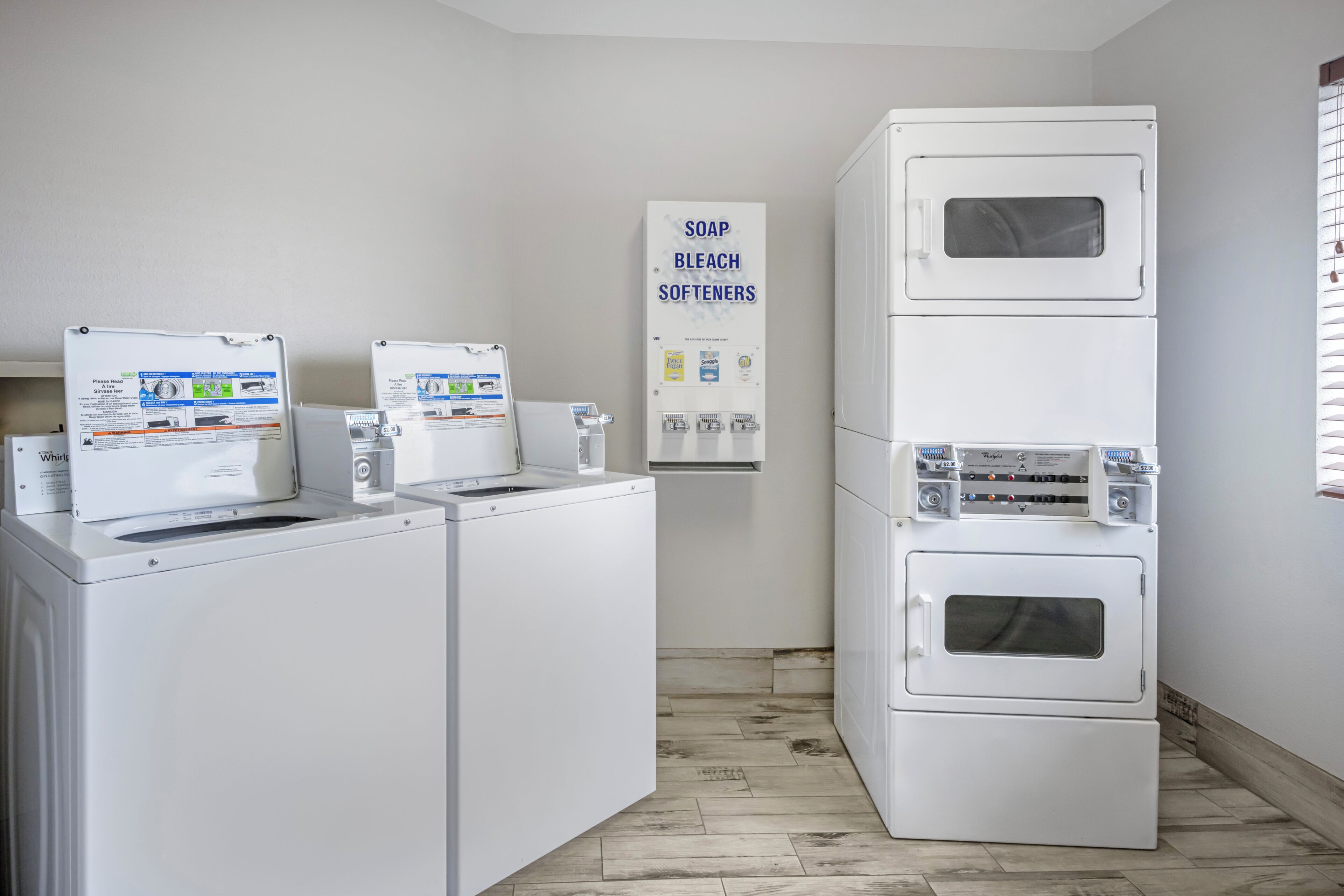 A laundry area with two front-loading washers, a stacked dryer, and a sign for soap, bleach, and softeners.