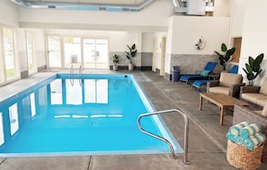 An indoor swimming pool with clear water, surrounded by lounge chairs and a wicker sofa.