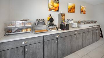 Um balcão de café da manhã com diversas opções de alimentos, uma máquina de waffles e uma cafeteira.