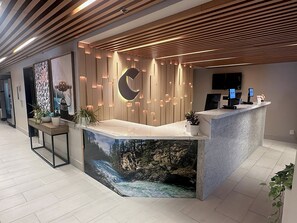 A modern reception desk with a wooden panel design, a large wall-mounted crescent moon light, and a digital screen. - Comfort Inn & Suites Post Falls - Coeur dAlene West (Post Falls)