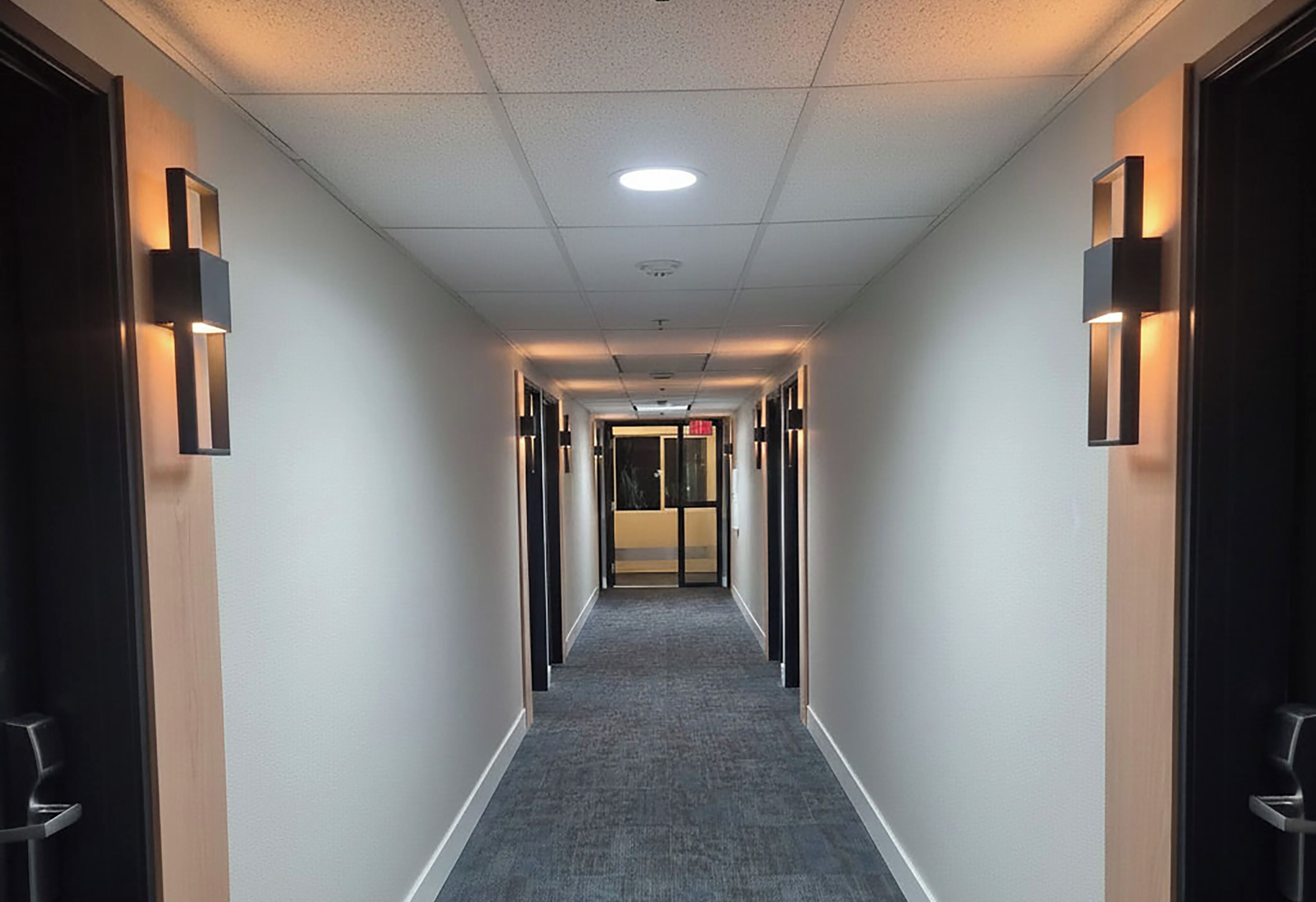 Un pasillo de hotel con piso alfombrado, iluminación empotrada y puertas a ambos lados.