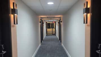 Un pasillo de hotel con piso alfombrado, iluminación empotrada y puertas a ambos lados.