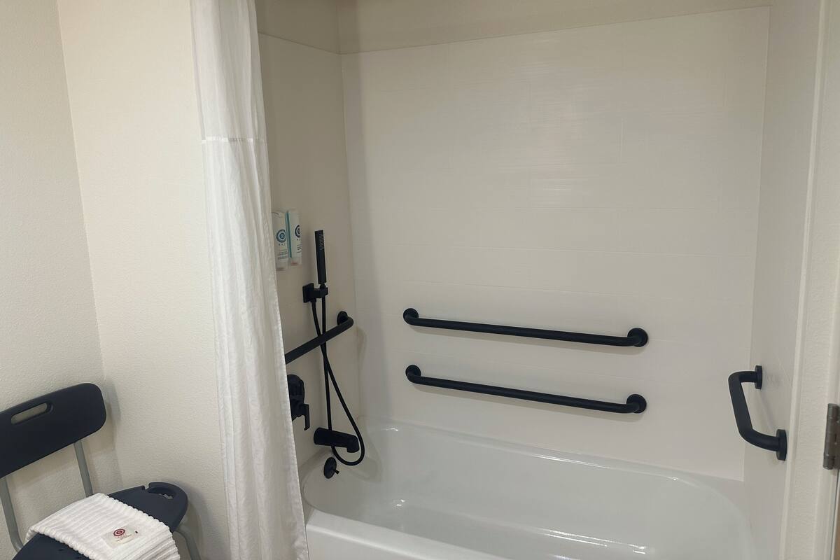 A bathroom with a white bathtub, a shower area, and a chair with a towel.