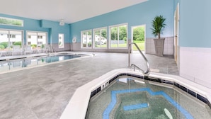 A swimming pool area with a tiled deck, a diving board, and a view of a residential neighborhood through large windows.
