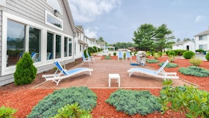 A house with a patio area featuring sun loungers and a table, surrounded by landscaped gardens and a clear sky.
