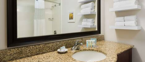 Un baño con lavamanos de granito, un espejo grande y estantes blancos para toallas.