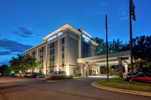 A modern hotel with a prominent "Hampton Inn" sign, a covered entrance, and a parking lot with several cars. - Hampton Inn Raleigh/Cary (Cary)