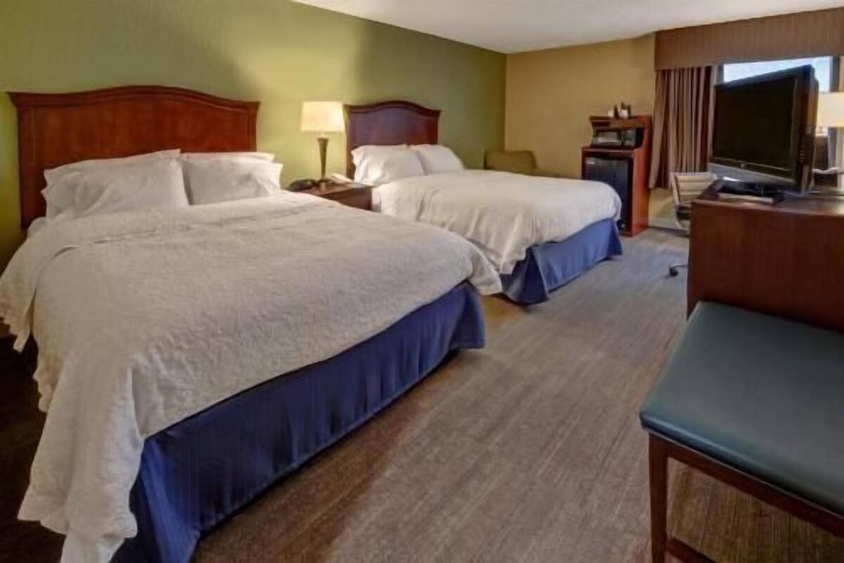 Ein Hotelzimmer mit zwei Betten, einem Fernseher, einem Schreibtisch und einem Stuhl.
