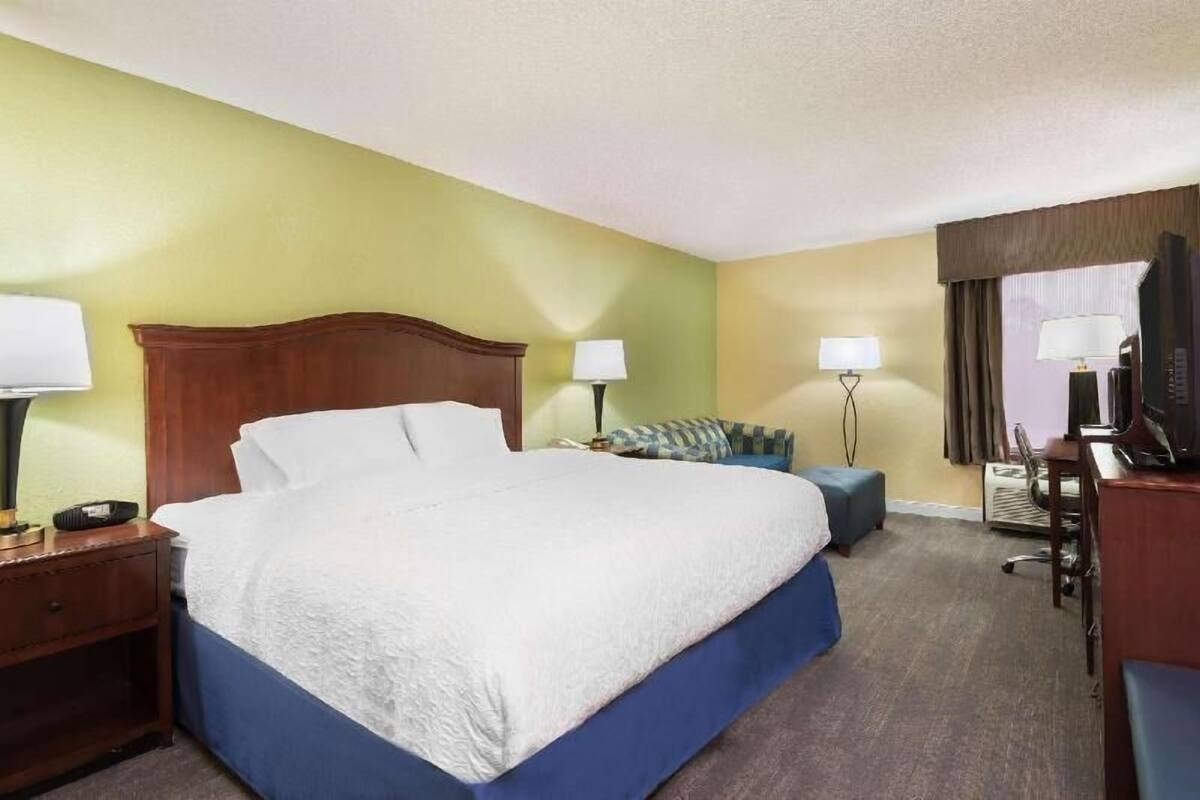 Ein Hotelzimmer mit einem großen Bett, Nachttischen, einem Schreibtisch mit Stuhl und einem Fernseher.