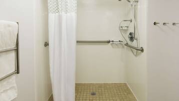 A shower area with a grab bar, a white curtain, and a tiled floor.