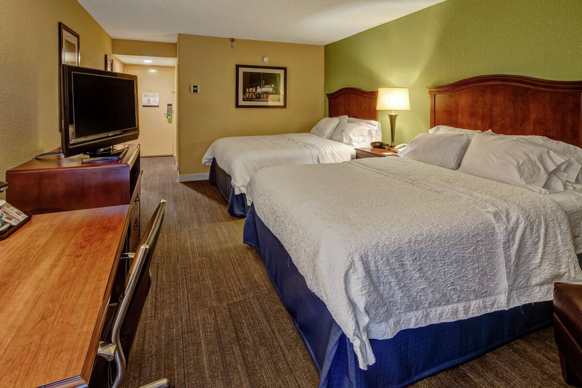 Ein Hotelzimmer mit zwei Betten, einem Fernseher und einem Schreibtisch.