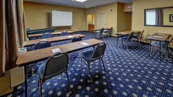 A conference room with a projector screen, tables, chairs, and a carpeted floor.