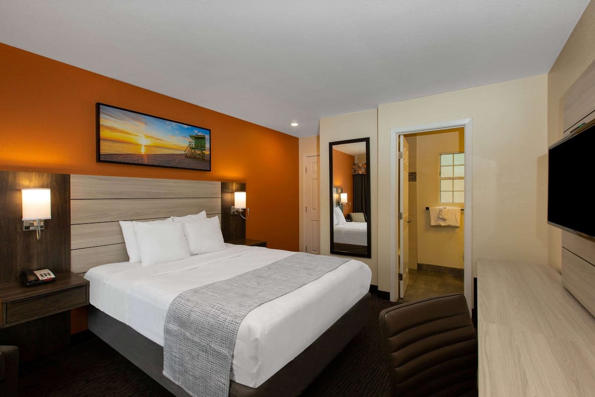 Habitación de hotel con una cama grande, una mesita de noche con un teléfono, un televisor montado en la pared y un cuadro sobre la cama.