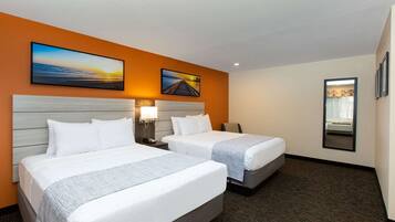 A hotel room with two beds, a large painting of a sunset, and a mirror on the wall.