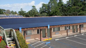 Un bâtiment doté d’un toit recouvert de panneaux solaires, un parking avec des places réservées aux personnes handicapées, et un escalier menant à une zone abritée.