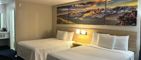 A hotel room with two beds, a large mountain landscape painting above the beds, and a nightstand with two wall-mounted lamps.