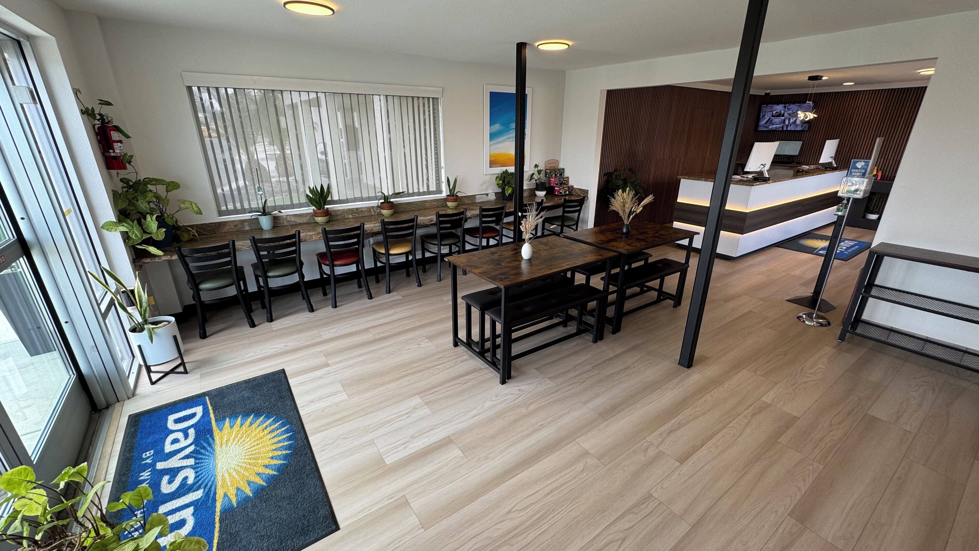 A modern hotel lobby with a reception desk, seating area, and a large window with blinds.