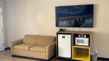 A small living area with a sofa, a mini-fridge, a microwave, and a TV mounted on the wall.