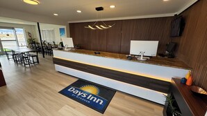 Ett välkomstområde med en receptionsdisk i trä, en modern lampa och utsikt över matsalen.