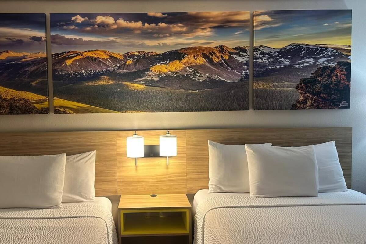 A hotel room with two beds, a wooden headboard, and a wall-mounted light fixture.