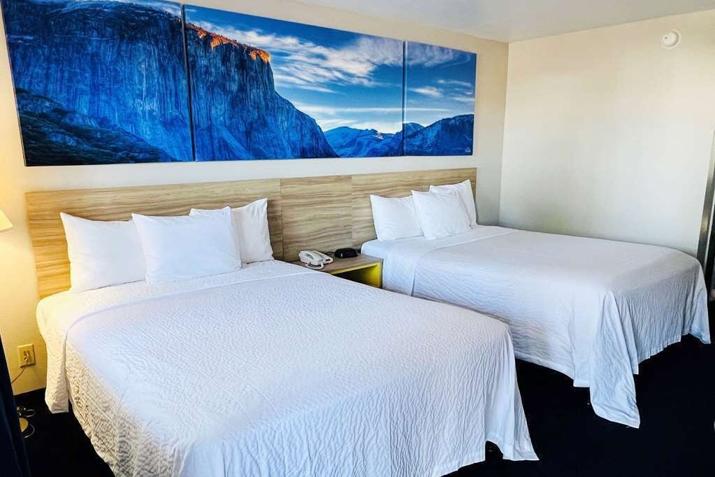 A hotel room with two beds, a wooden headboard, a large painting of a mountain landscape, and a nightstand with a phone.