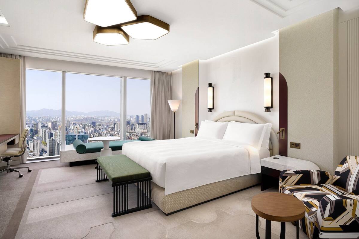 Habitación de hotel con una cama grande, un escritorio, una silla, un banco y vistas a la ciudad.