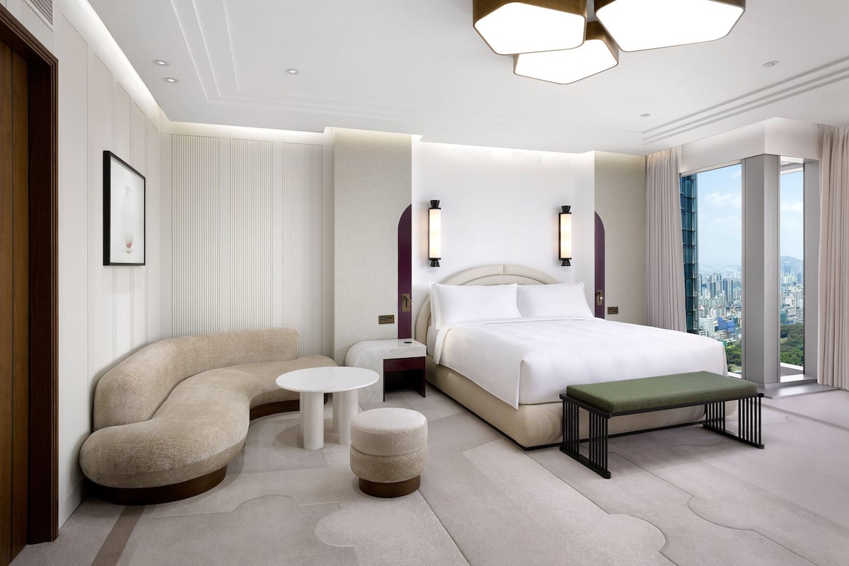 Una habitación de hotel moderna con un sofá curvo, una mesa redonda, un banco y una cama grande con vista a la ciudad.