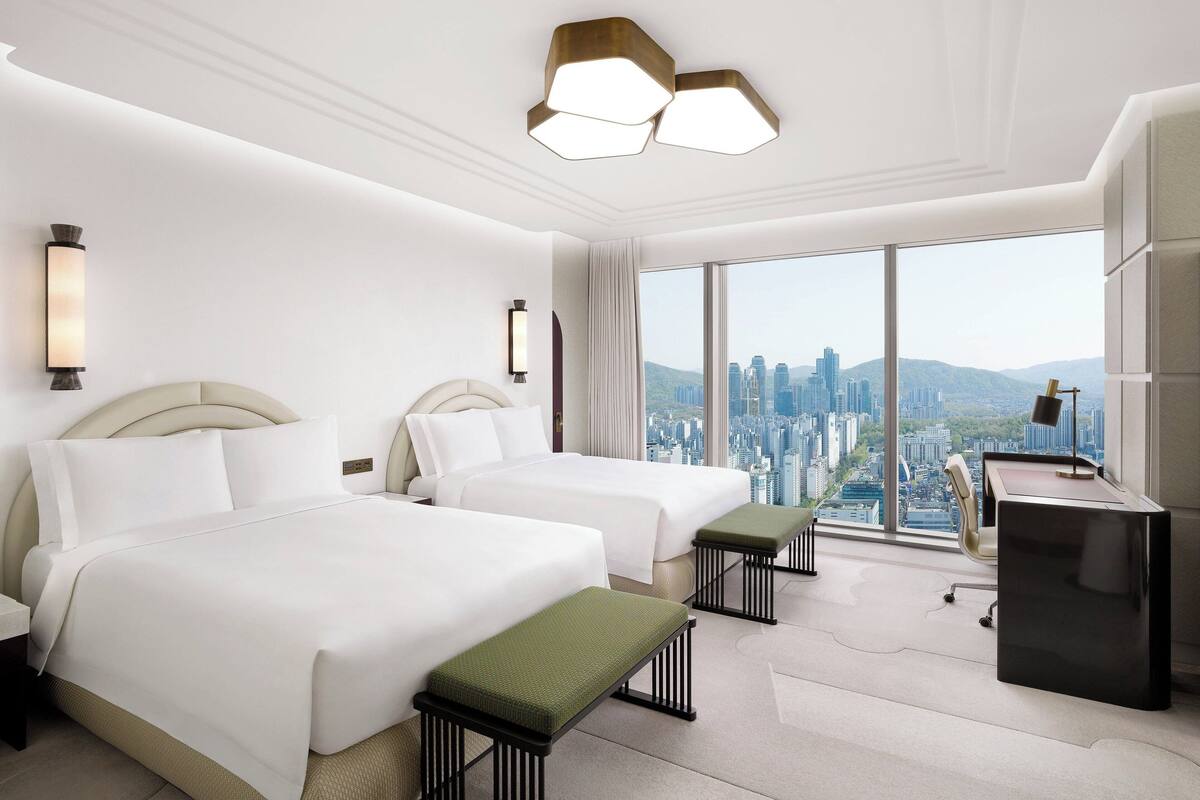 Habitación de hotel con dos camas, un escritorio y un ventanal con vistas a la ciudad.