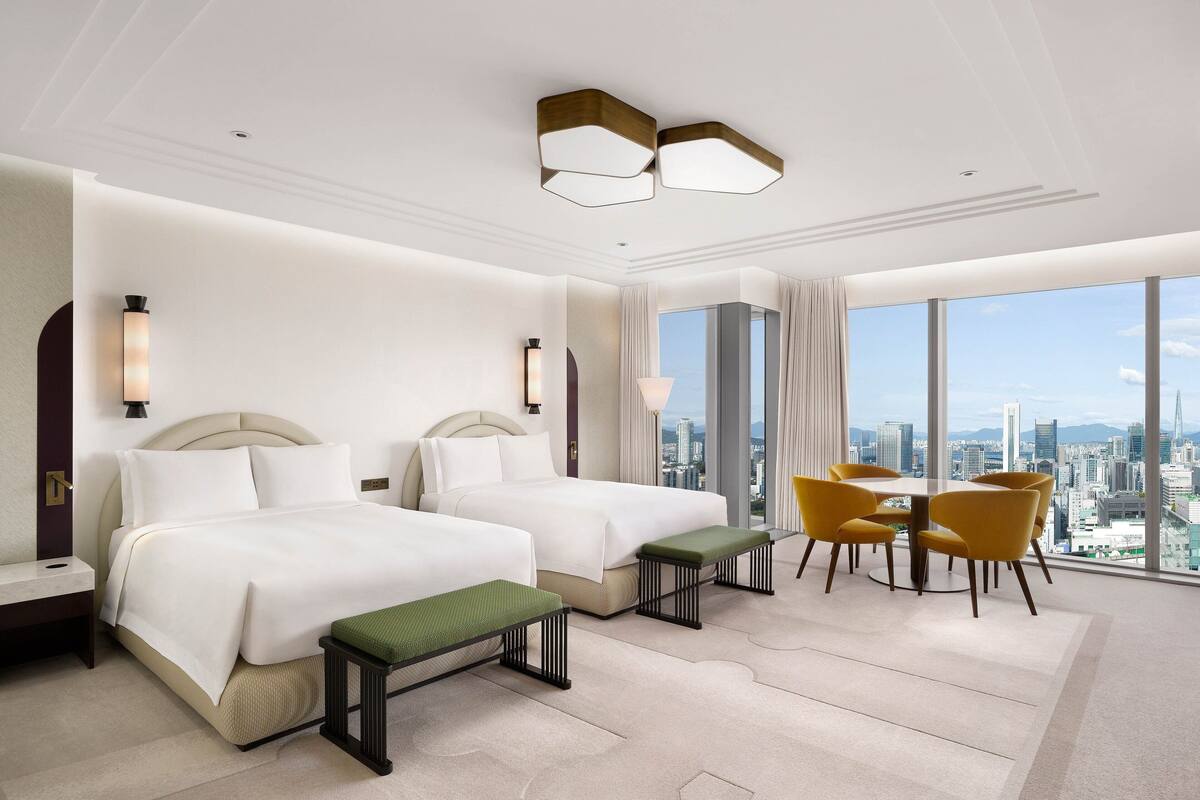 Una habitación de hotel moderna con dos camas, una zona de comedor y vistas a la ciudad.