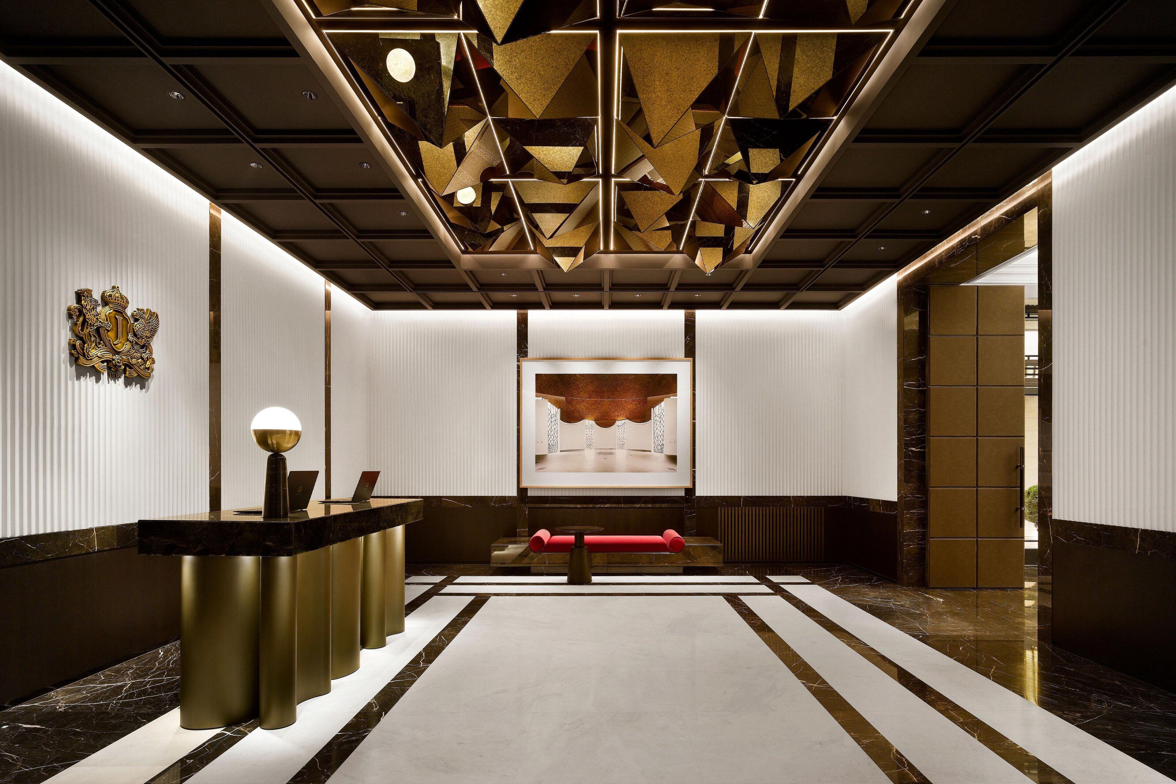 A modern hotel lobby with a reception desk, a large abstract artwork on the wall, and a patterned floor.