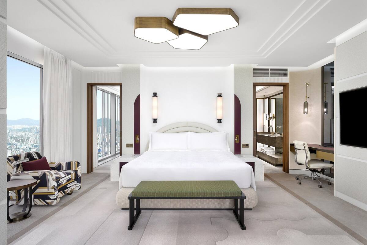Habitación de hotel moderna con una cama grande, un banco, un escritorio y vistas a la ciudad.