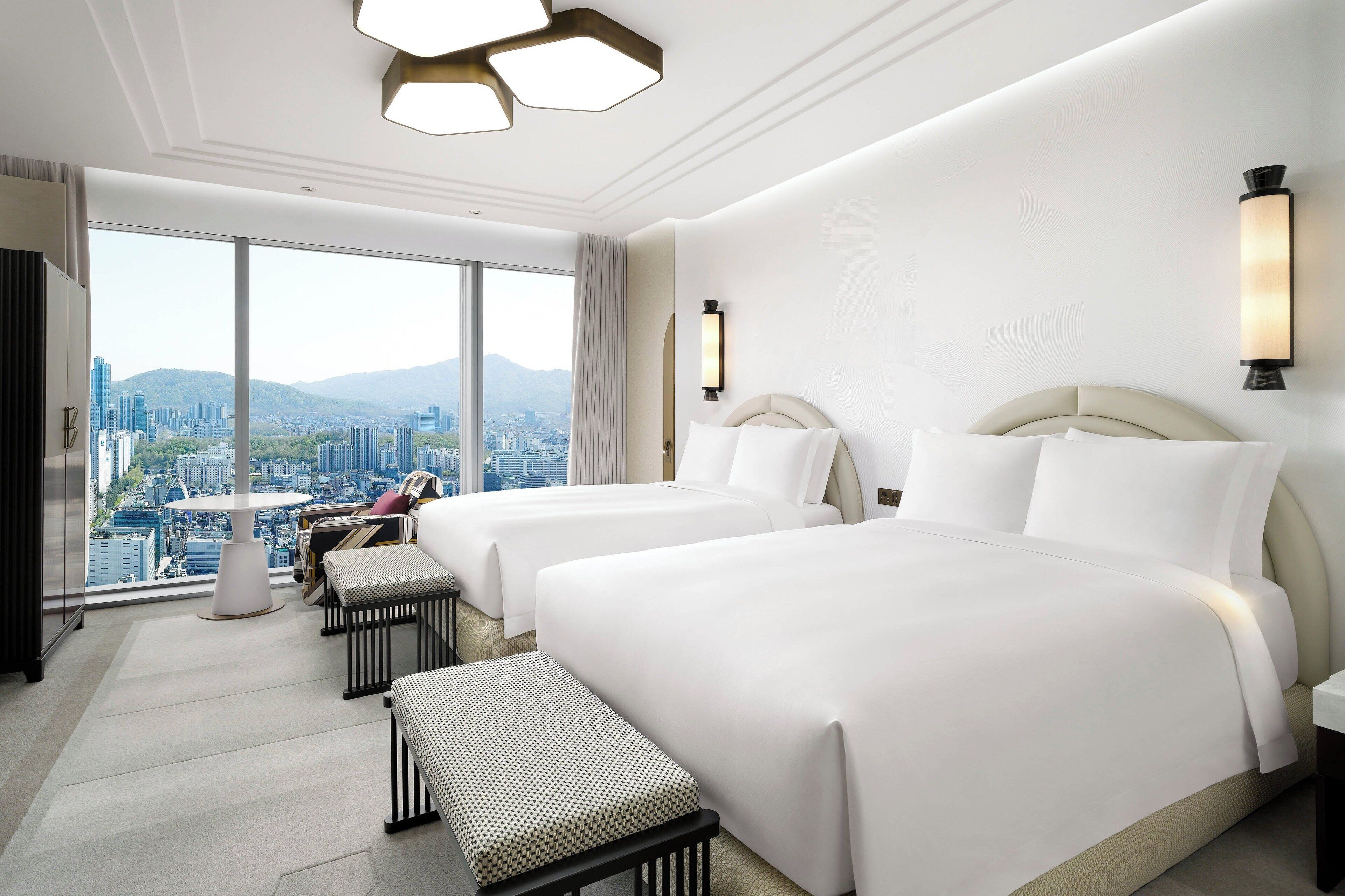 A hotel room with two beds, a sofa, a small table, and a view of a cityscape.
