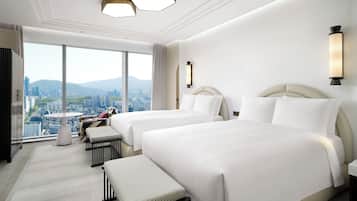A hotel room with two beds, a sofa, a small table, and a view of a cityscape.
