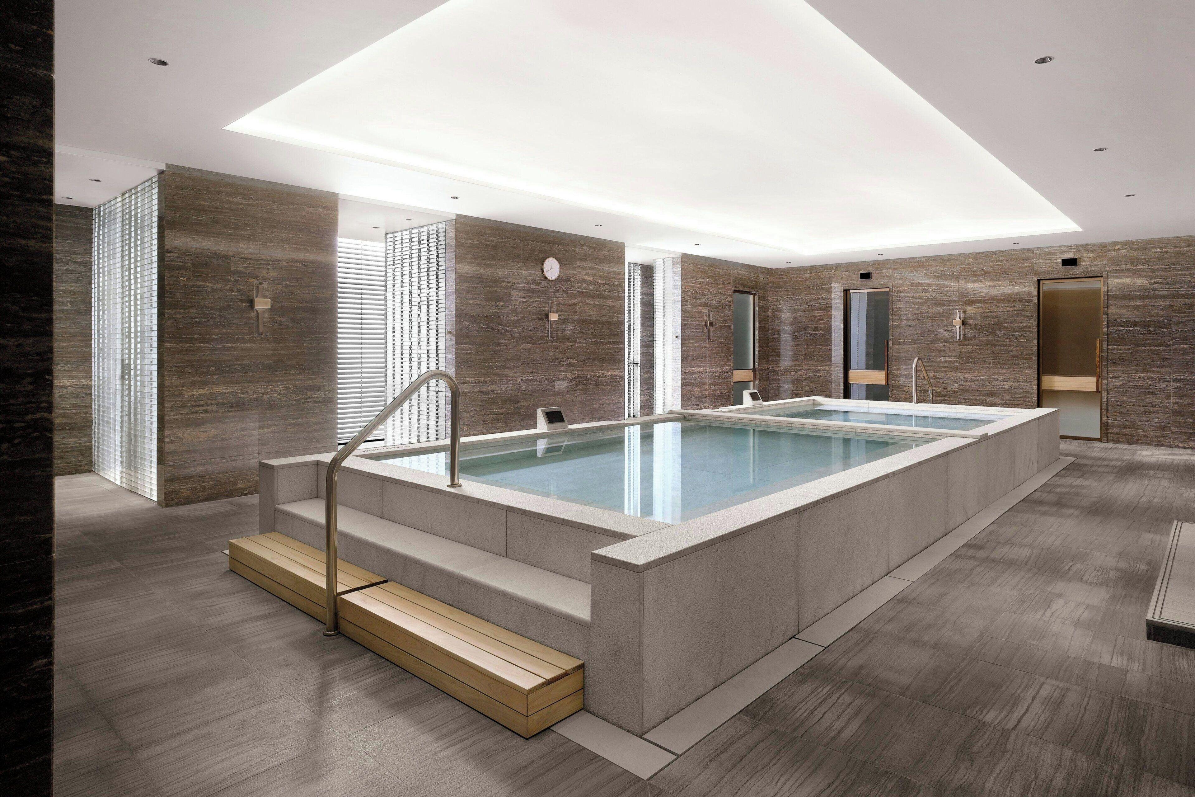 A modern indoor swimming pool with a skylight, stone walls, and a minimalist design.