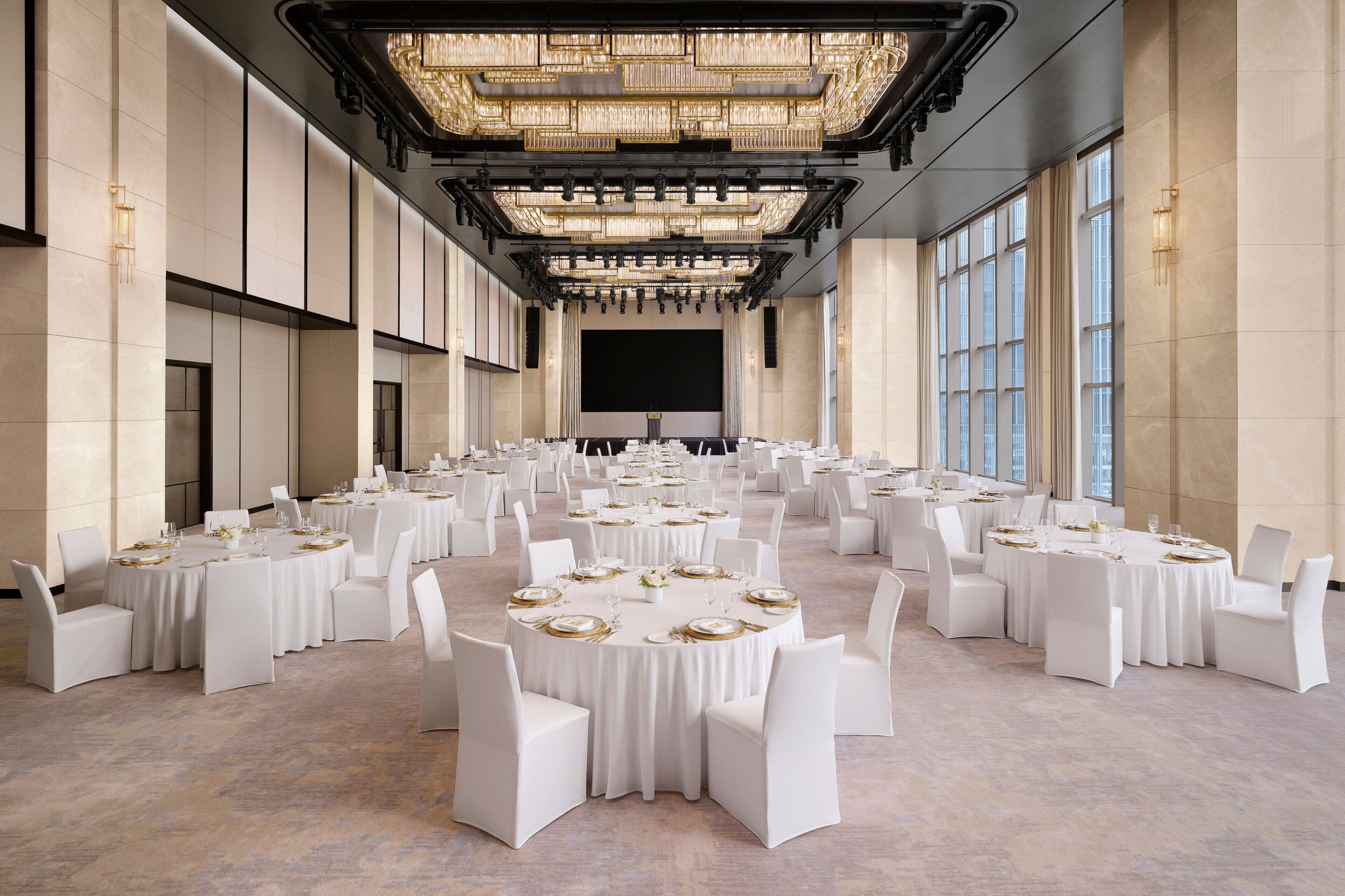 A large banquet hall with round tables set for dining, featuring white chairs and gold accents.