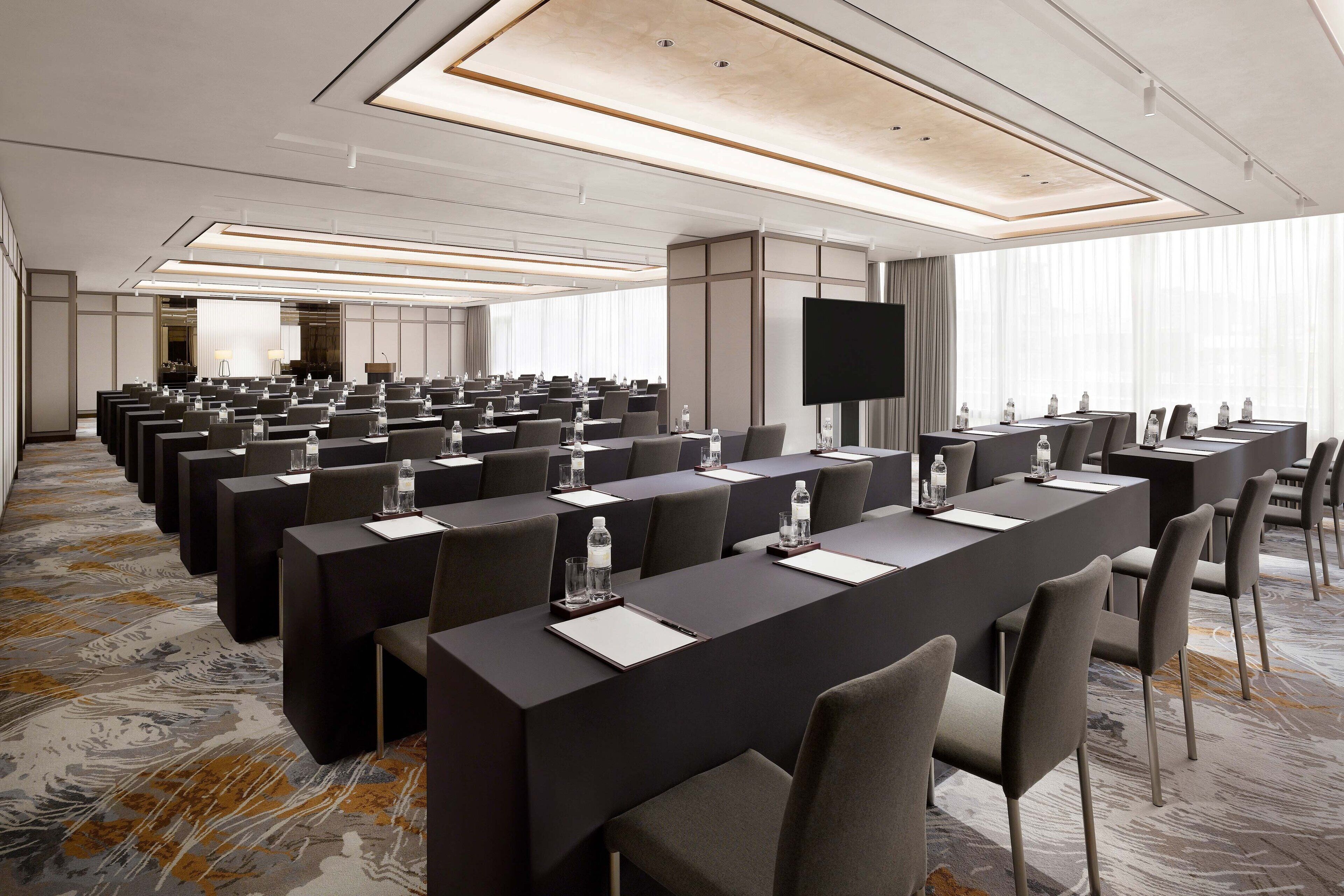 Un salón de conferencias con largas mesas, sillas y una pantalla grande.