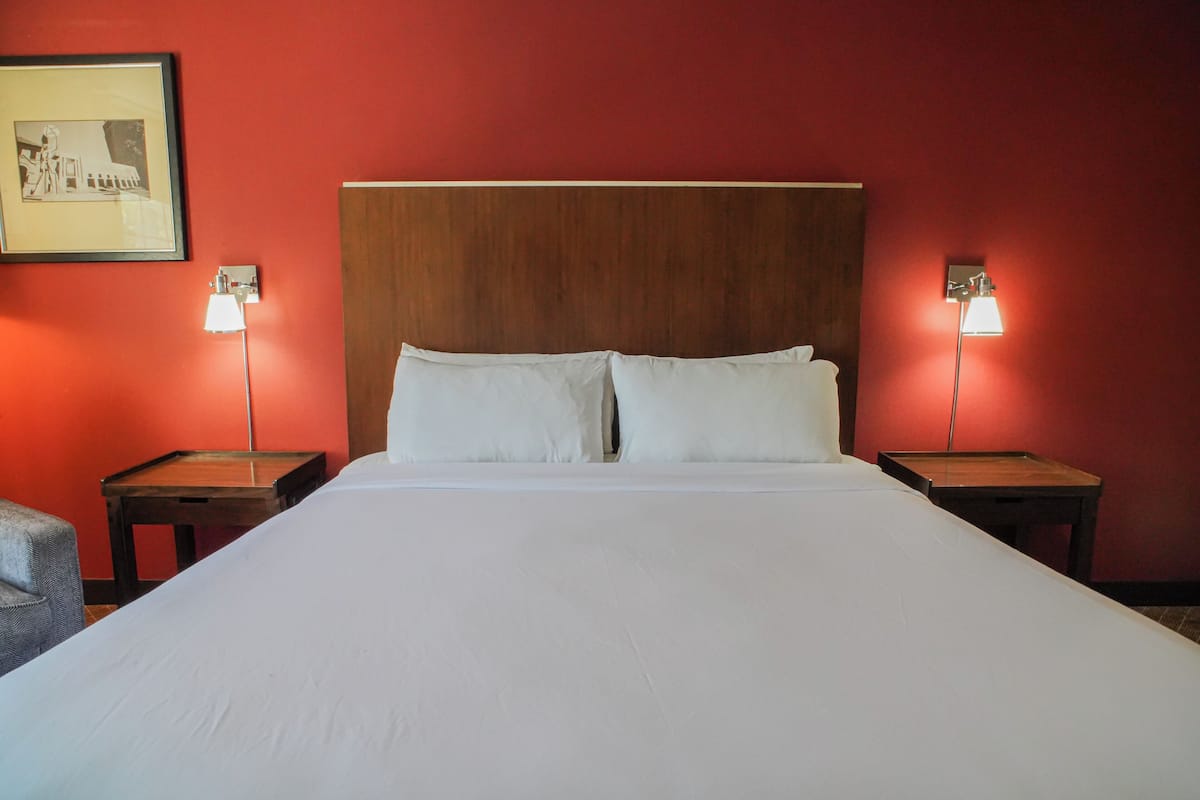 A hotel room with a large bed, two bedside tables, and two wall-mounted lamps.