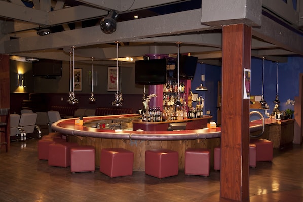 A bar area with a curved counter, multiple stools, and a television mounted on the wall.