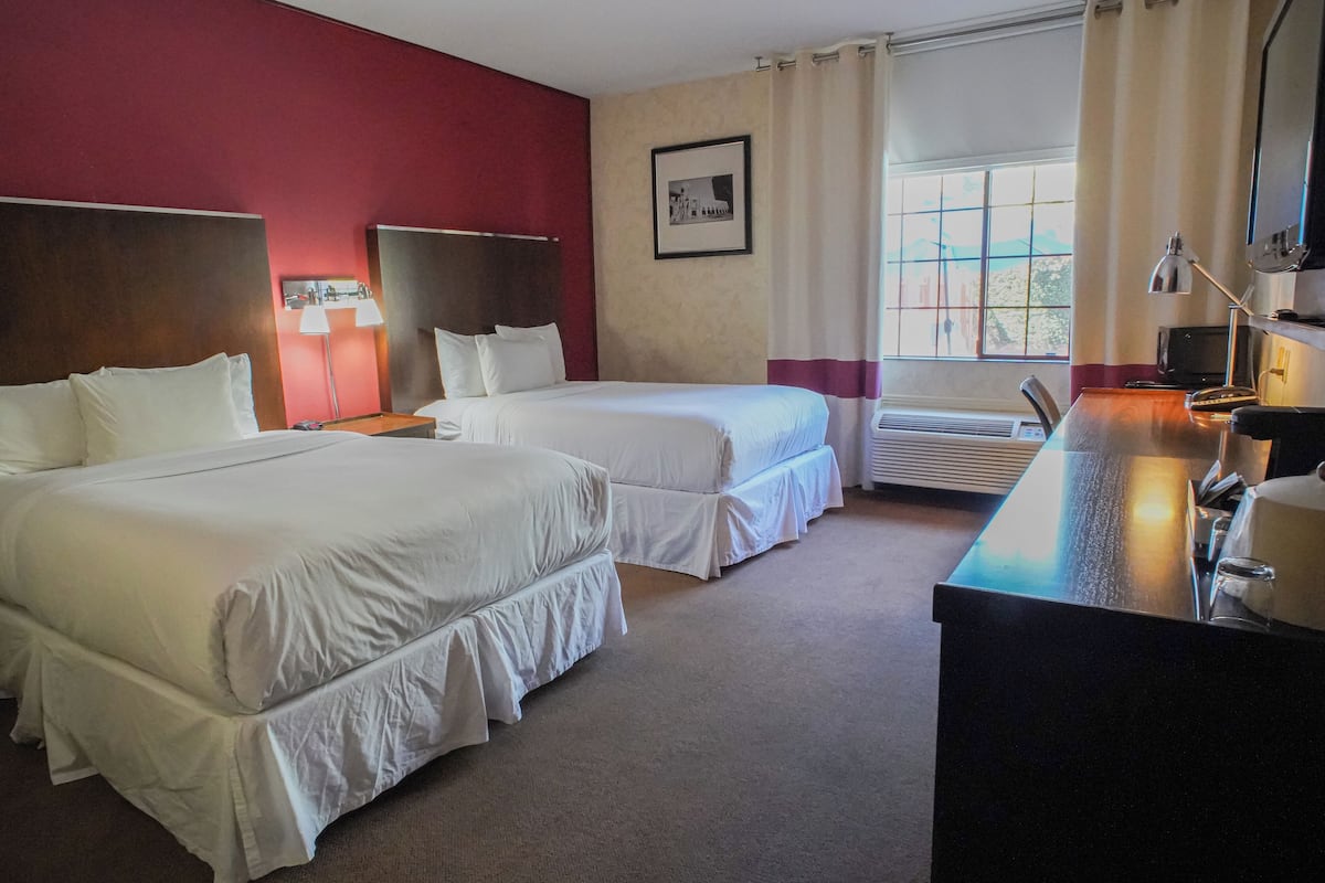 A hotel room with two beds, a desk, a chair, a lamp, a picture on the wall, and a window with curtains.
