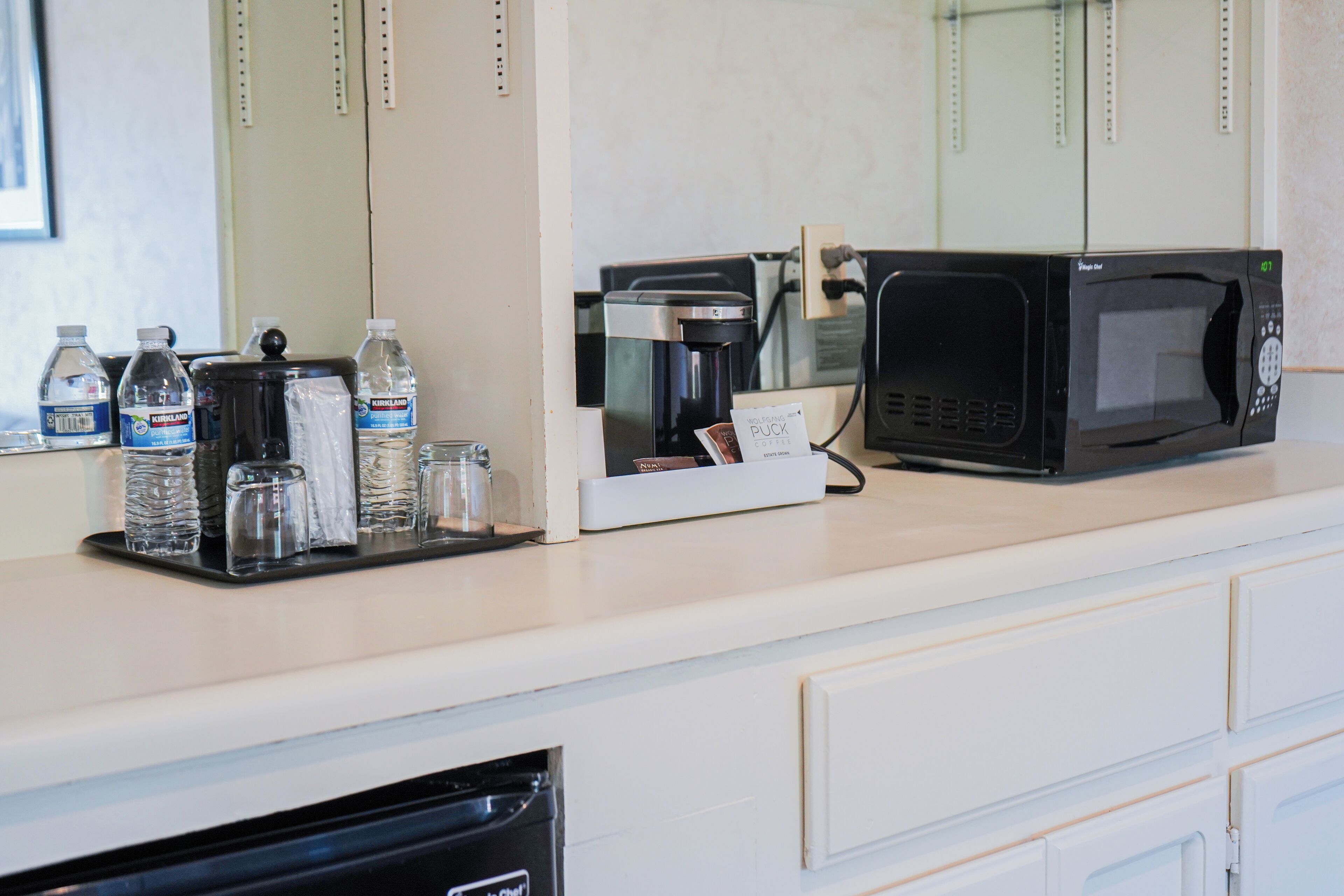 A kitchenette with a coffee maker, microwave, water bottles, and salt and pepper shakers.