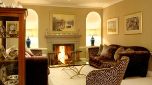 A living room with a fireplace, two armchairs, a sofa, and a patterned armchair. - Wentworth Hotel (Aldeburgh)