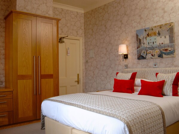 Habitación de hotel con un armario grande, una cama con ropa de cama roja y blanca, un cuadro en la pared y una lámpara.